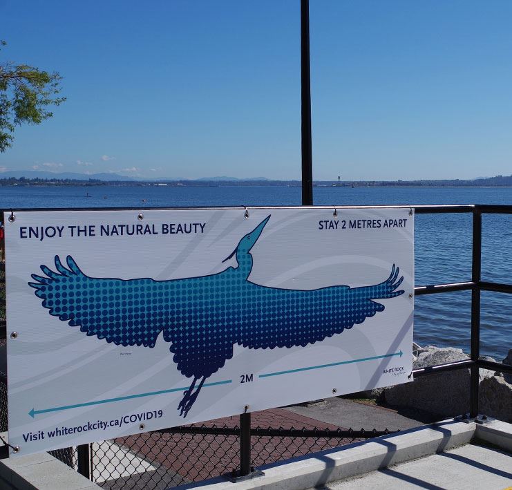 Blue heron sign at White Rock Waterfront reminding visitors to stay 2 metres apart.