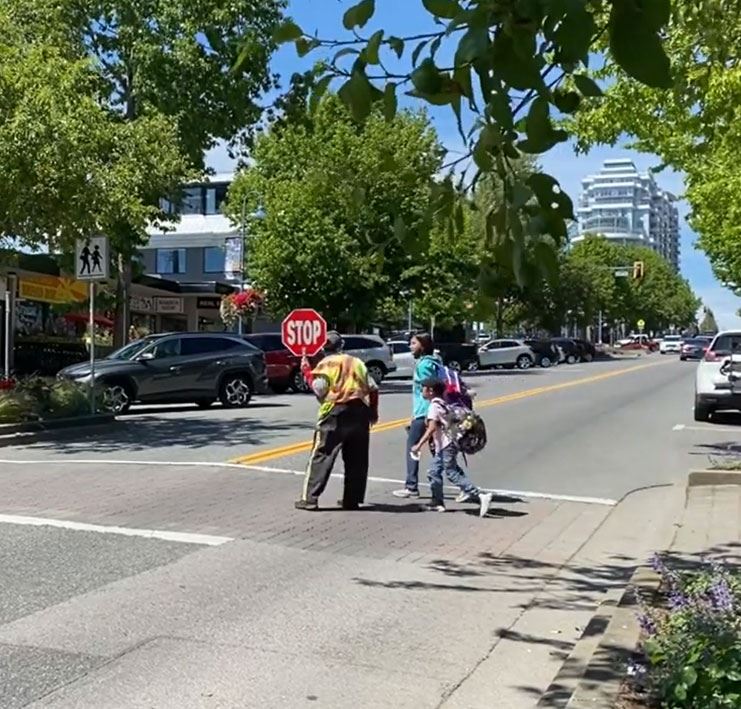 Crossing guard holding stop sign, parent walking across street with child
