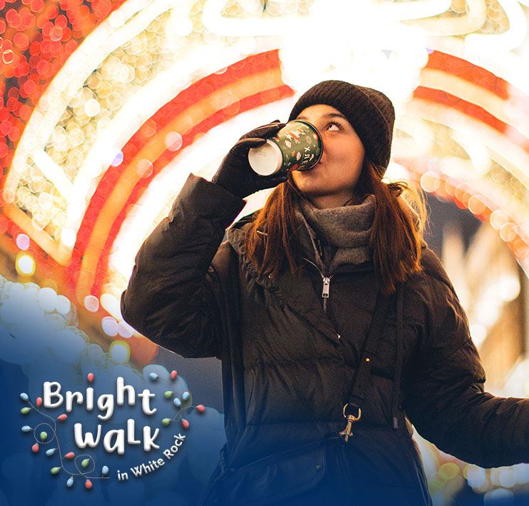 woman walking under Christmas lights drinking hot chocolate