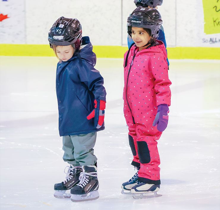 two kids wearing helmets and ice skates on ice