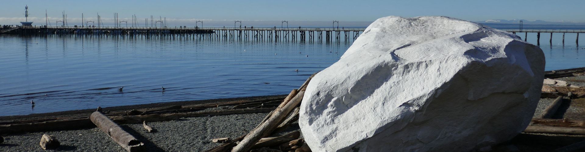 White rock on beachfront with wooden pier in background