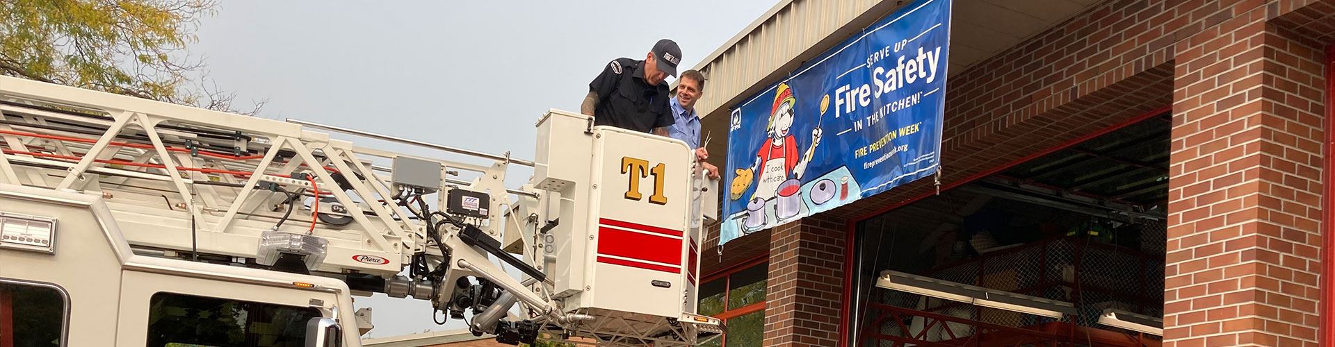 Firefighters on truck ladder installing fire prevention week banner